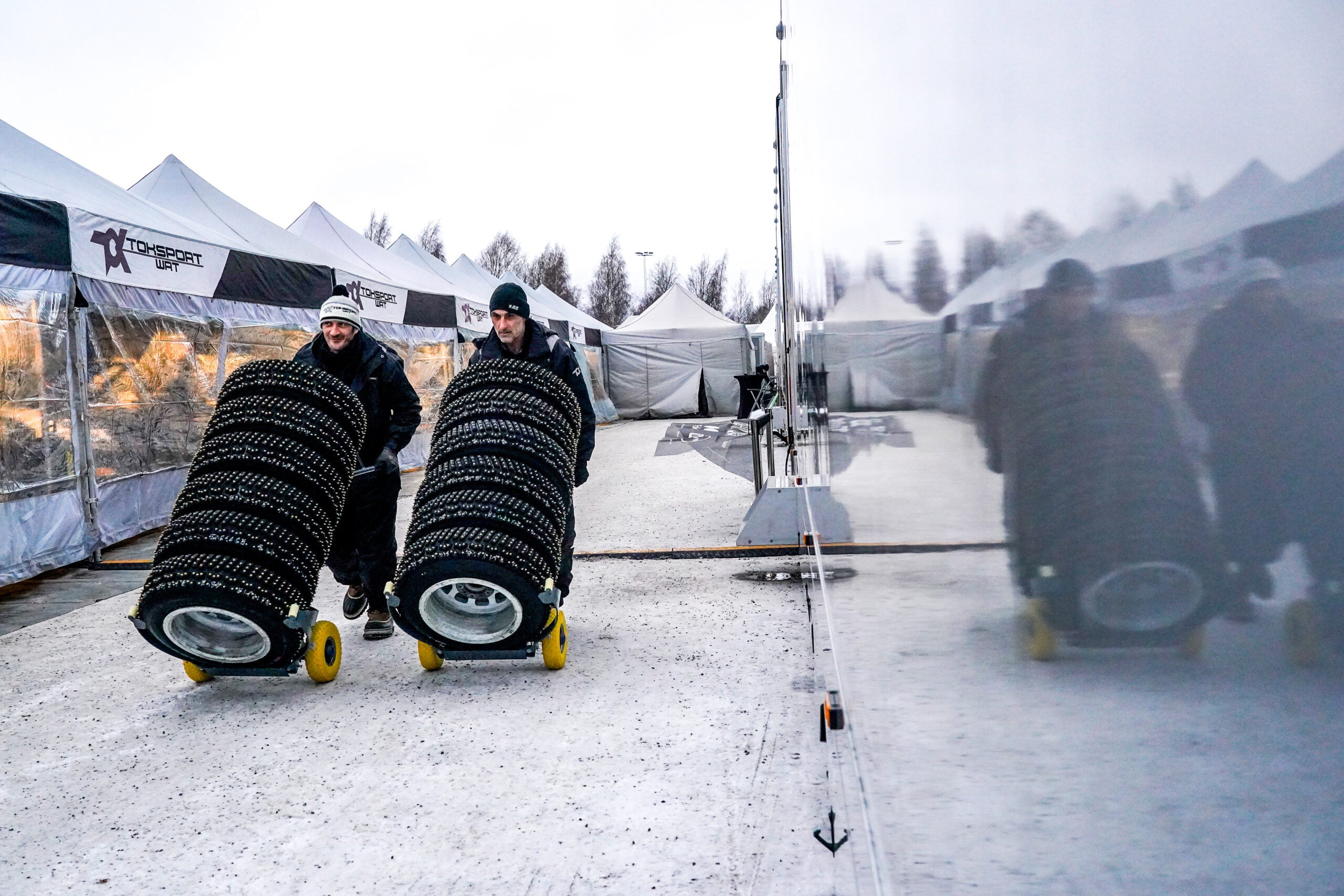 Two technicians using Gaither Smart Carts to transport studded tires outdoors at a racing event