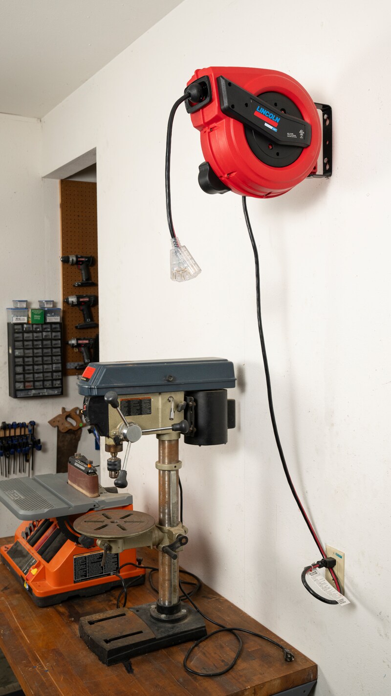 Lincoln Industrial 91039 retractable electric cord reel wall-mounted above drill press in garage workshop