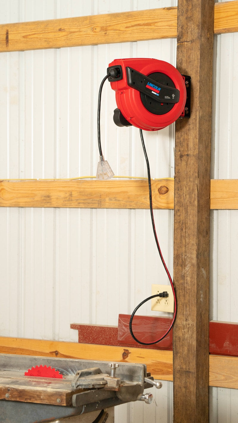Lincoln Industrial 91039 retractable cord reel mounted on workshop wall with table saw below