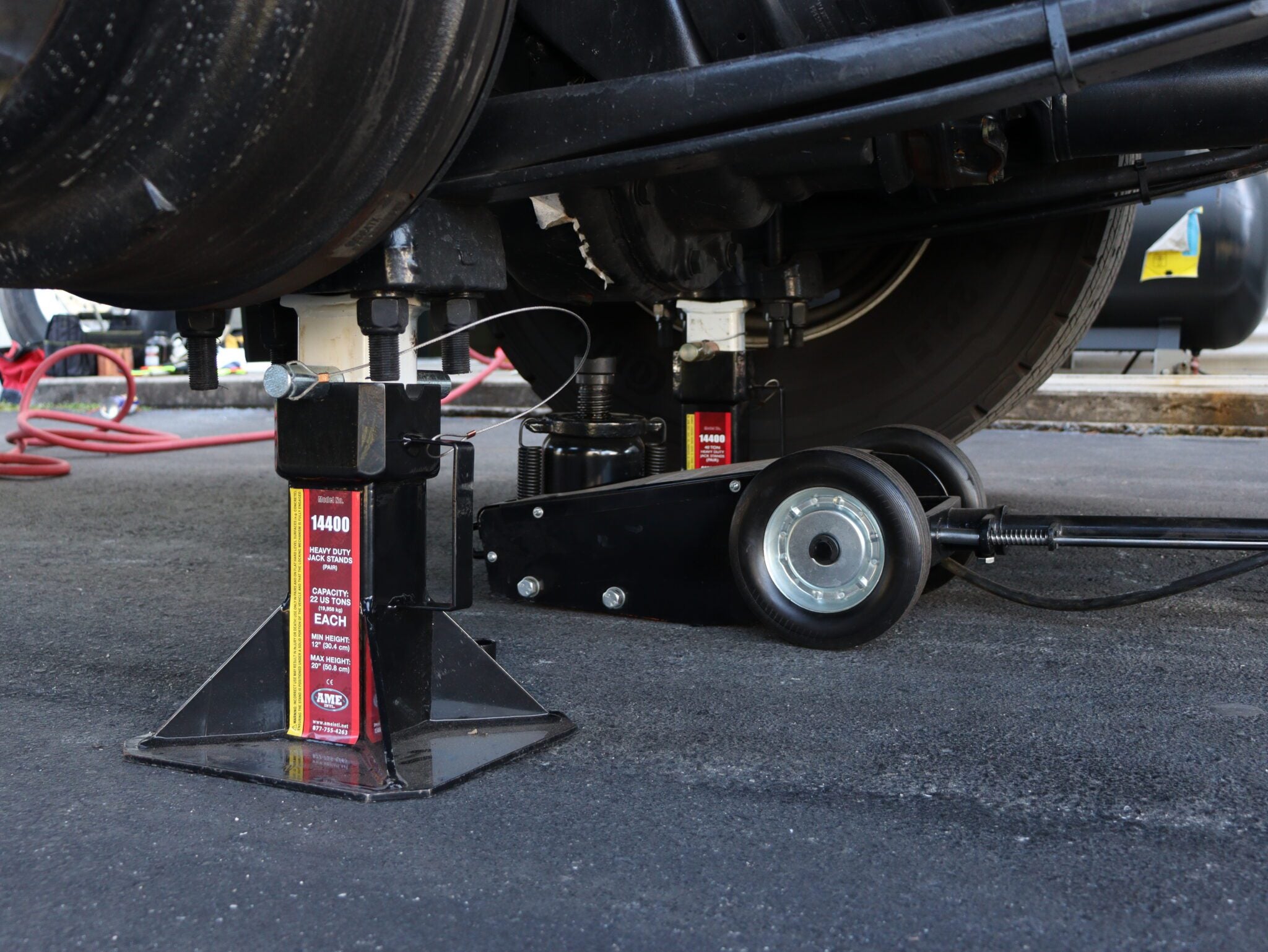 AME International 14400 22-Ton Heavy Duty Jack Stand in use under a commercial vehicle on a paved surface