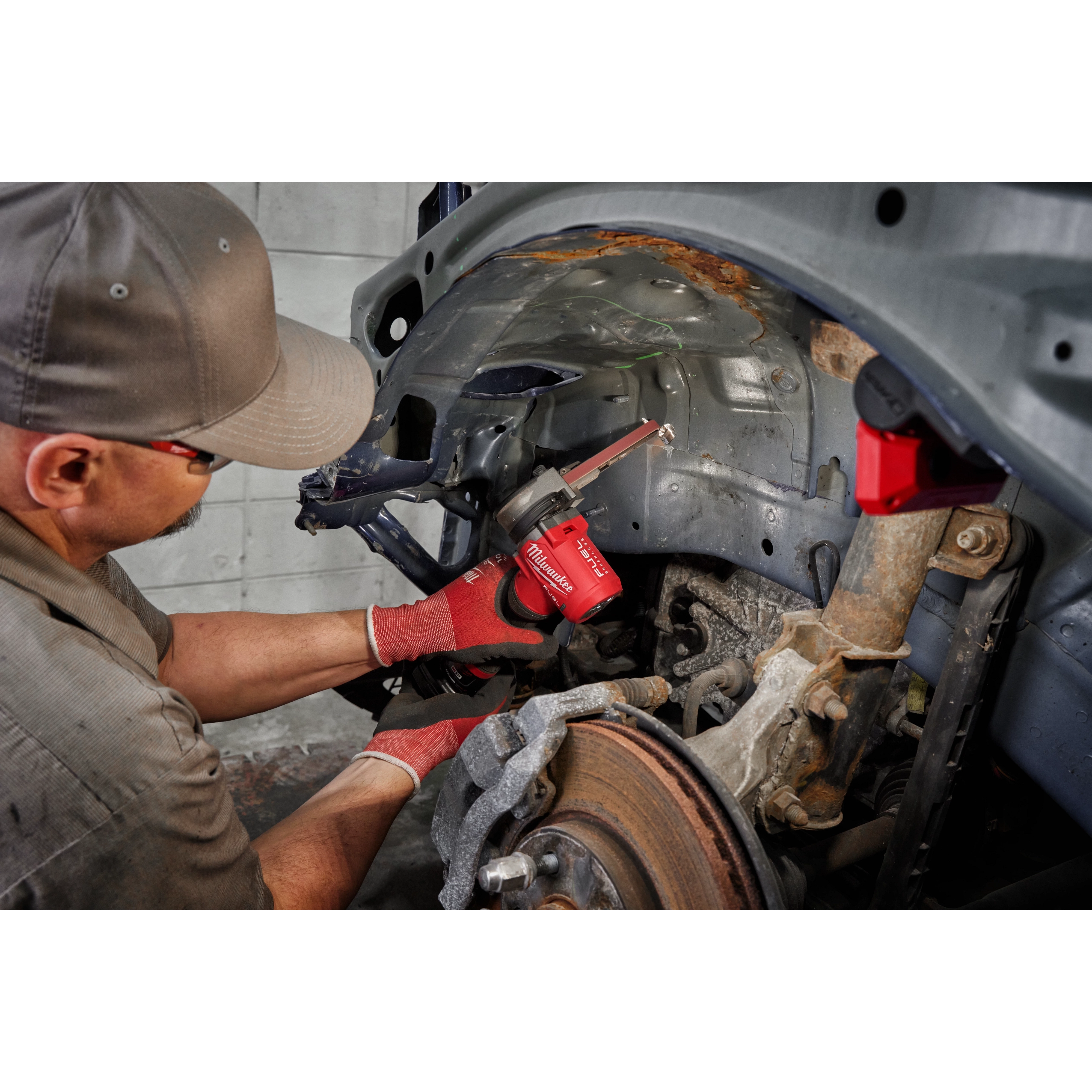 Mechanic using Milwaukee M12 FUEL Bandfile for automotive undercarriage rust removal