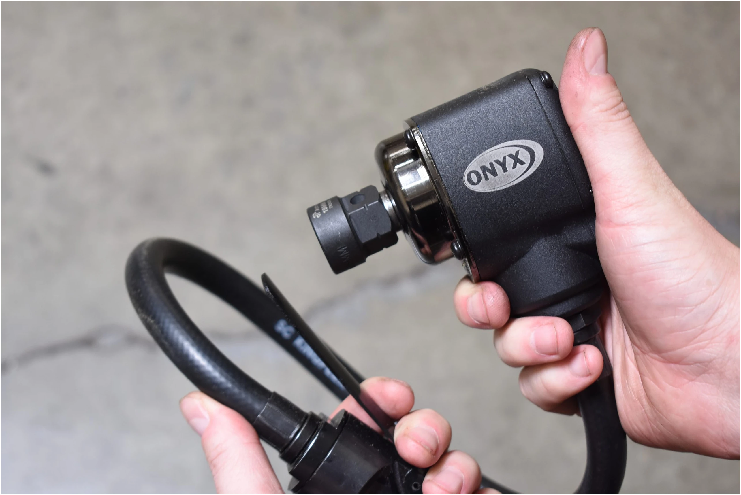 Astro Pneumatic ONYX 1/2 Inch Palm Impact Wrench close-up with socket and hose loop, in-use lifestyle shot
