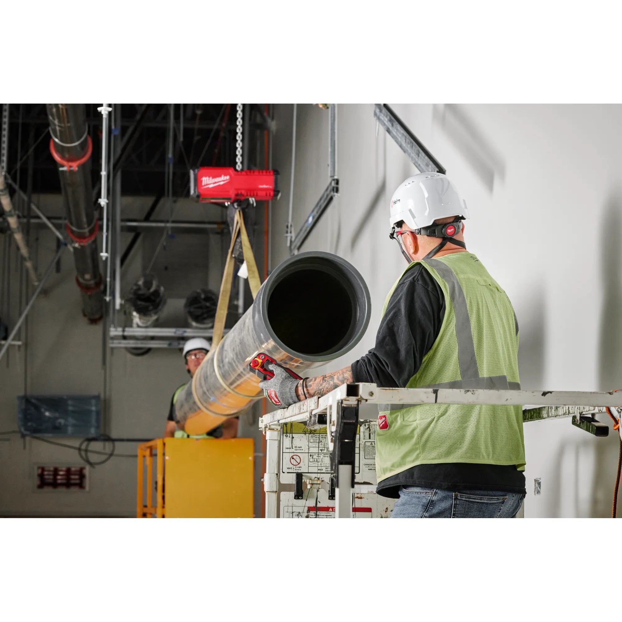 Two workers using Milwaukee M18 Chain Hoist to lift large duct pipe on a scissor lift at a job site