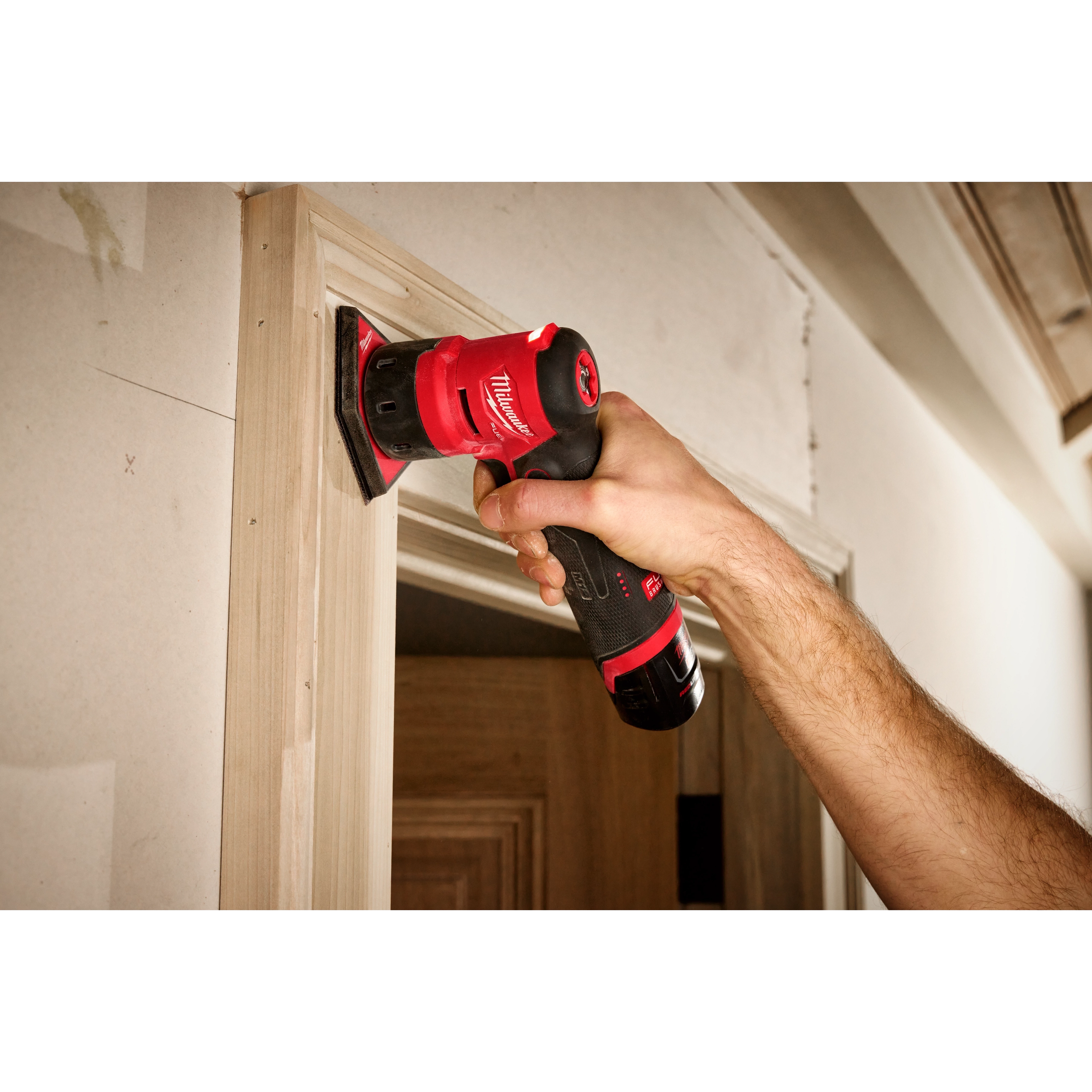 Milwaukee M12 FUEL Orbital Detail Sander in use sanding door trim on jobsite