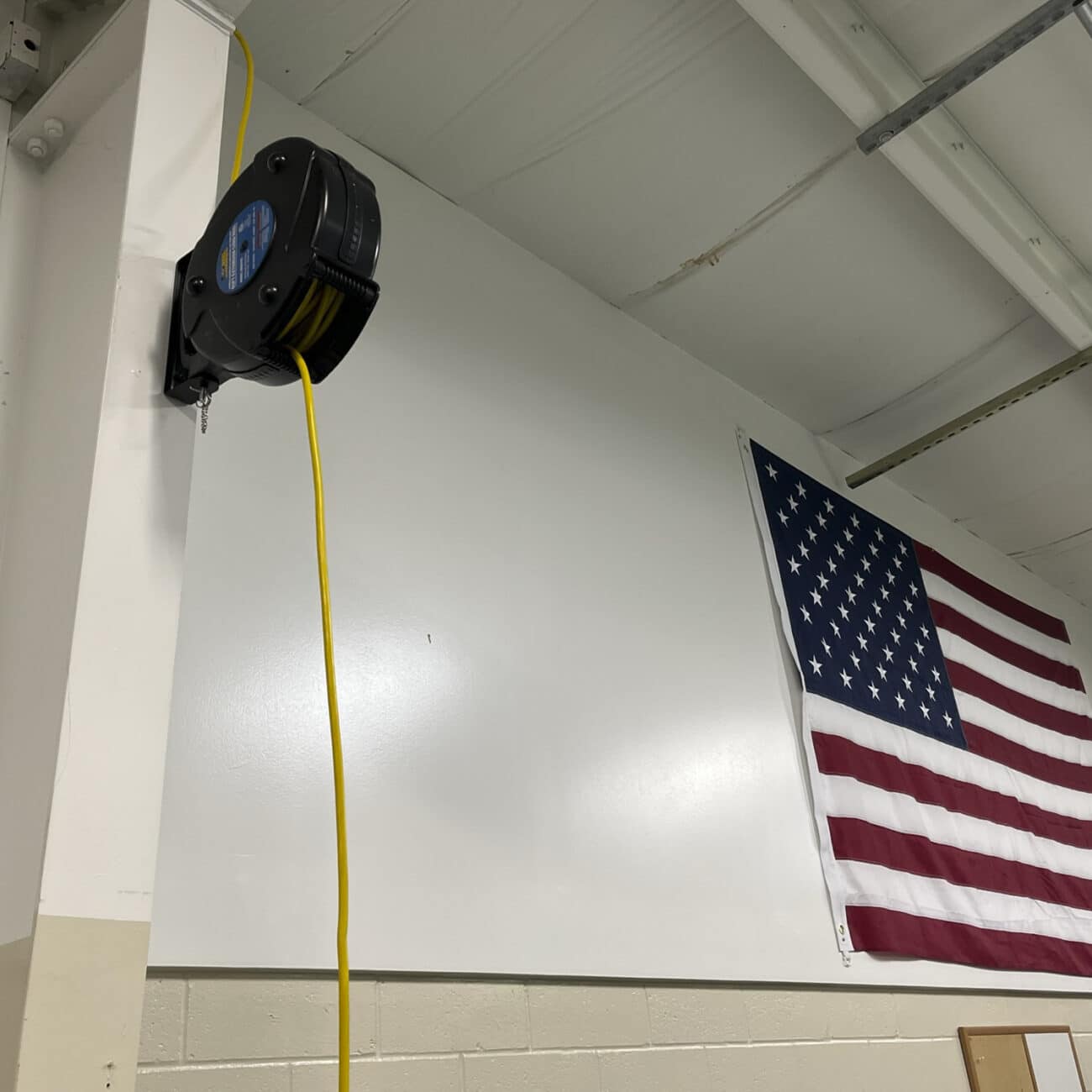 Alert Stamping 8665TFQ Retractable Cord Reel mounted on wall in garage with yellow cord extended