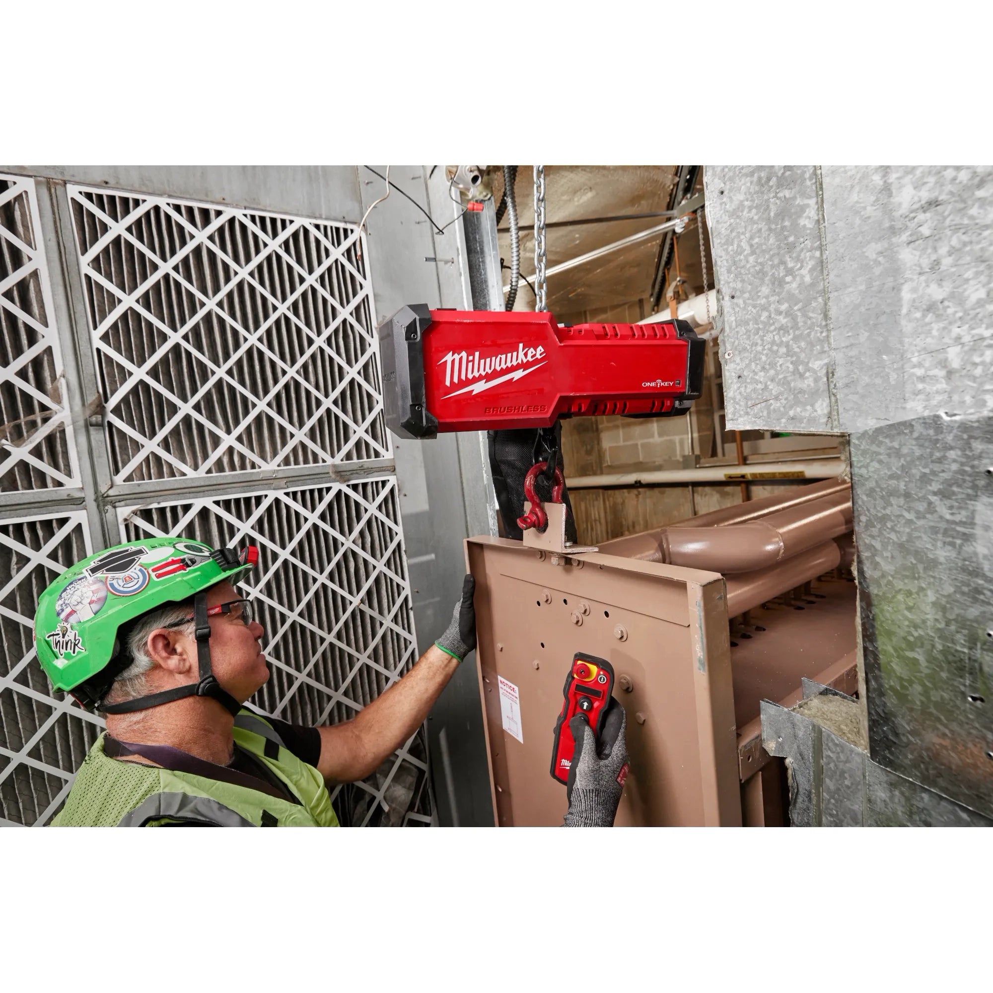 Worker using Milwaukee M18 Chain Hoist and wireless remote to lift HVAC equipment in tight space