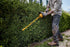 User trimming tall hedges with Dewalt DCHT870B 60V MAX Cordless Hedge Trimmer outdoors