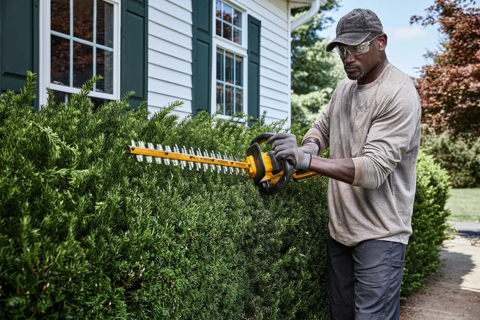 Man trimming bushes beside a house with Dewalt DCHT870B 60V MAX Cordless Hedge Trimmer