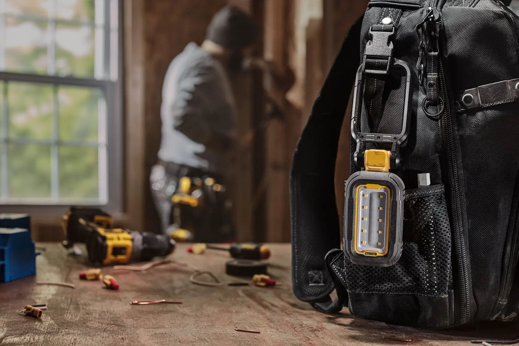 Dewalt DCL182 LED Task Light clipped to tool bag on jobsite with worker in background