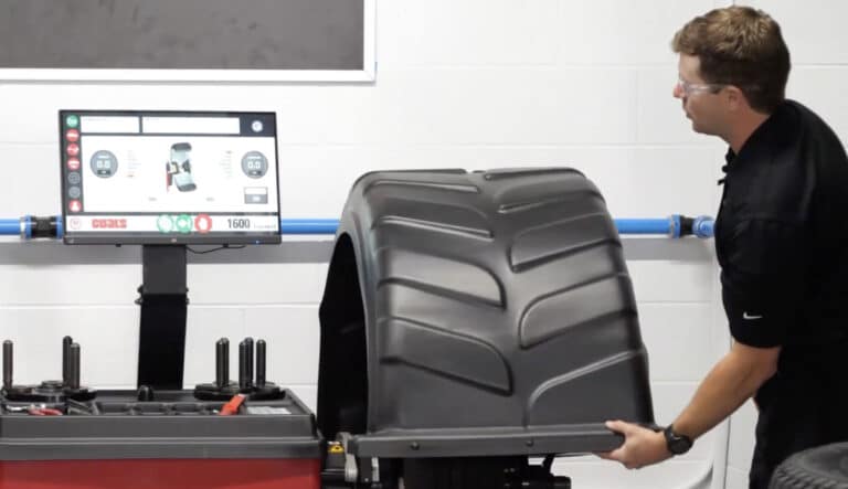 Technician positioning a large tire on the Coats 1600 wheel balancer with touchscreen visible