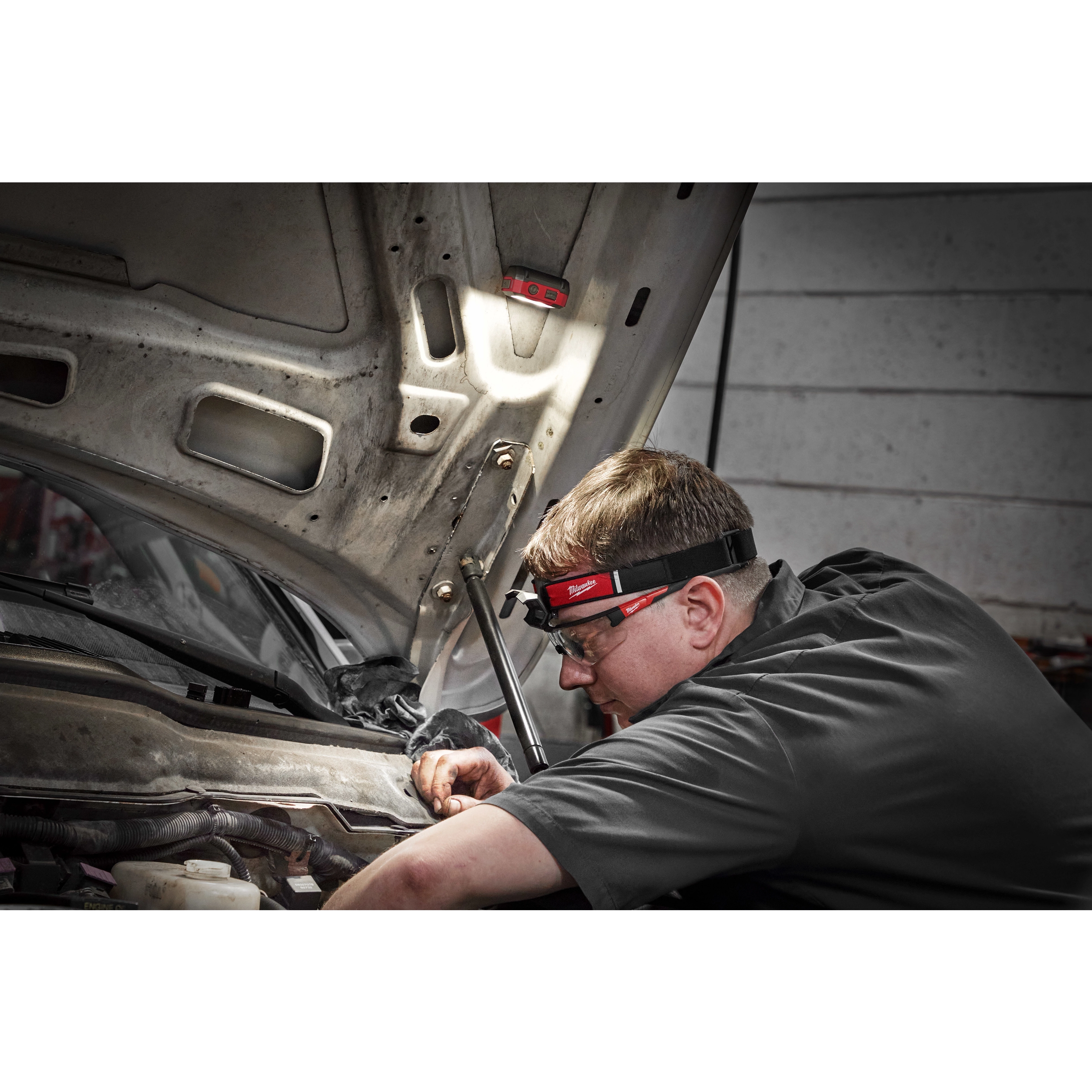Milwaukee Tool 2012R Rechargeable Magnetic Headlamp worn by mechanic working under vehicle hood