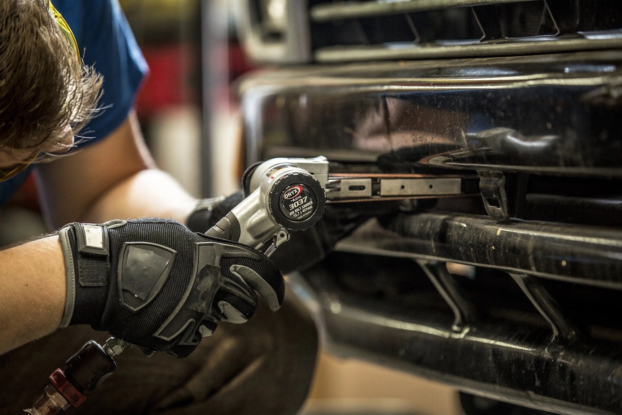 Technician using Astro Pneumatic 3037 Air Belt Sander on vehicle grille in auto shop