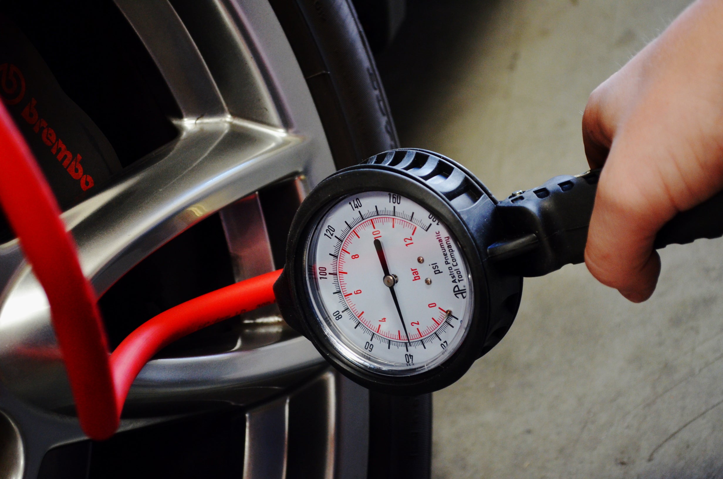 Astro Pneumatic AST-3081 Dial Gauge Tire Inflator in use measuring tire pressure on a performance car wheel