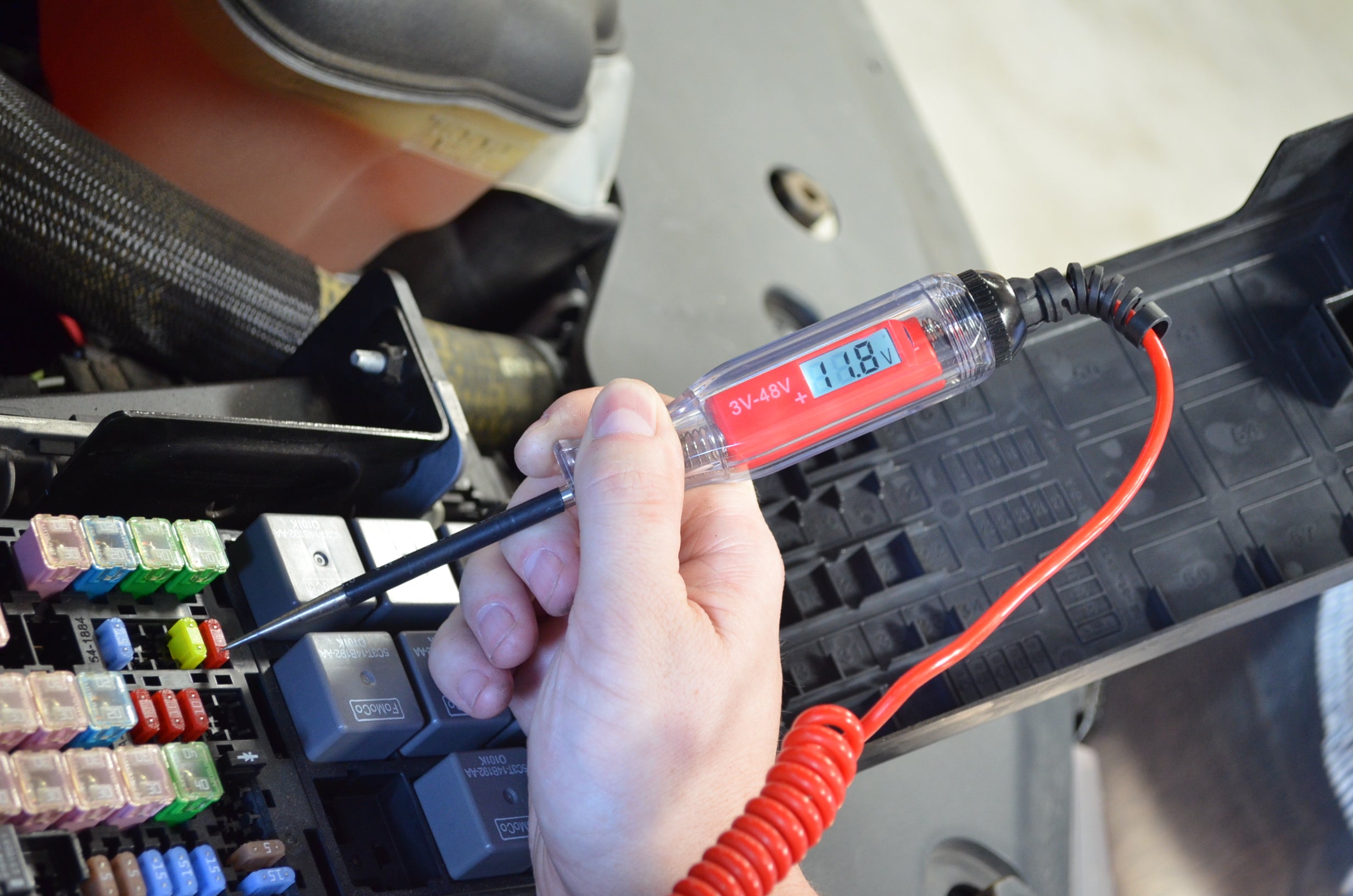 Astro Pneumatic AST-7764 circuit tester in use at vehicle fuse box showing 11.8V reading on LCD display