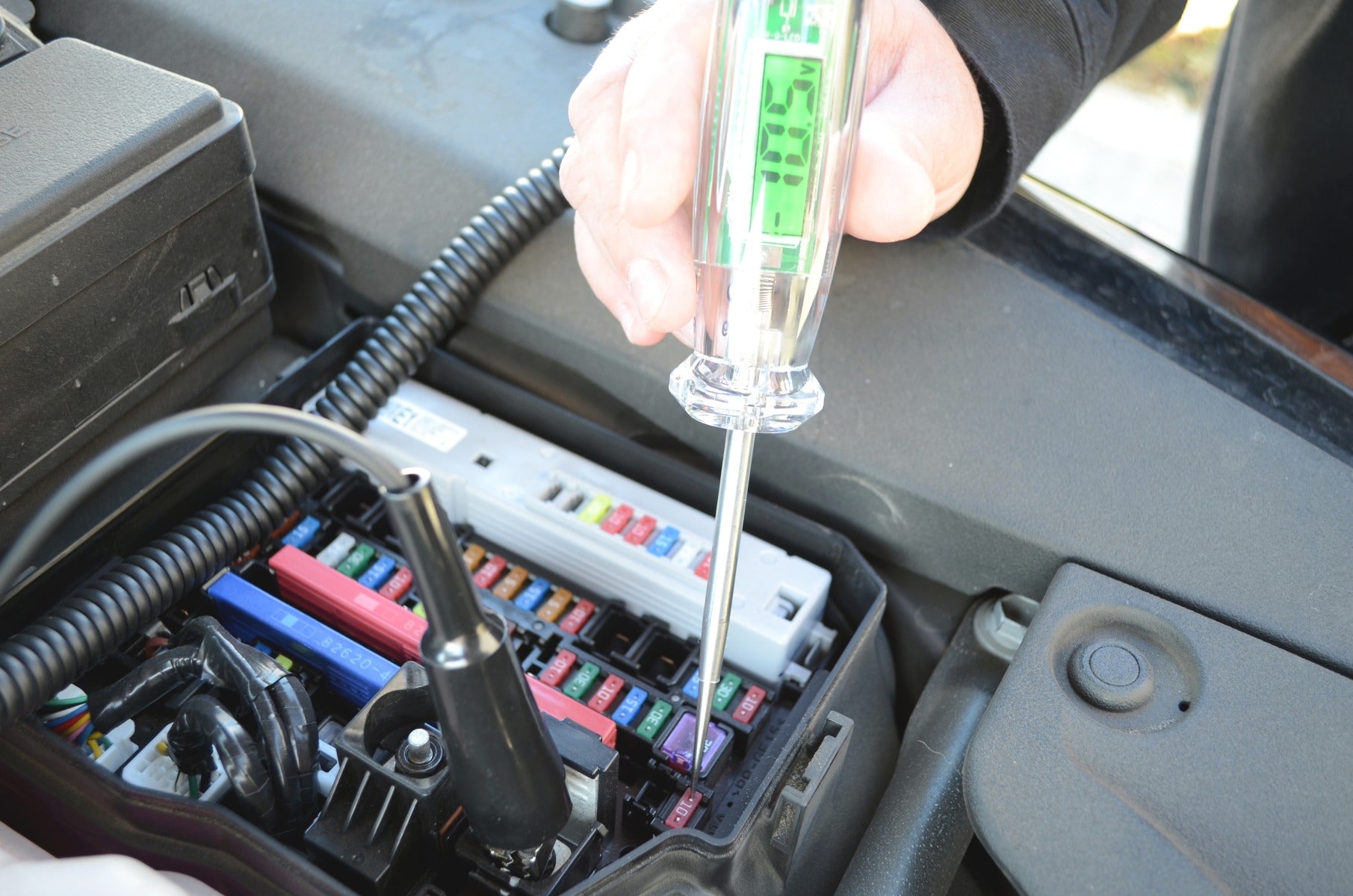 Astro Pneumatic 7767 Digital LCD Circuit Tester in use at vehicle fuse panel, lifestyle photo