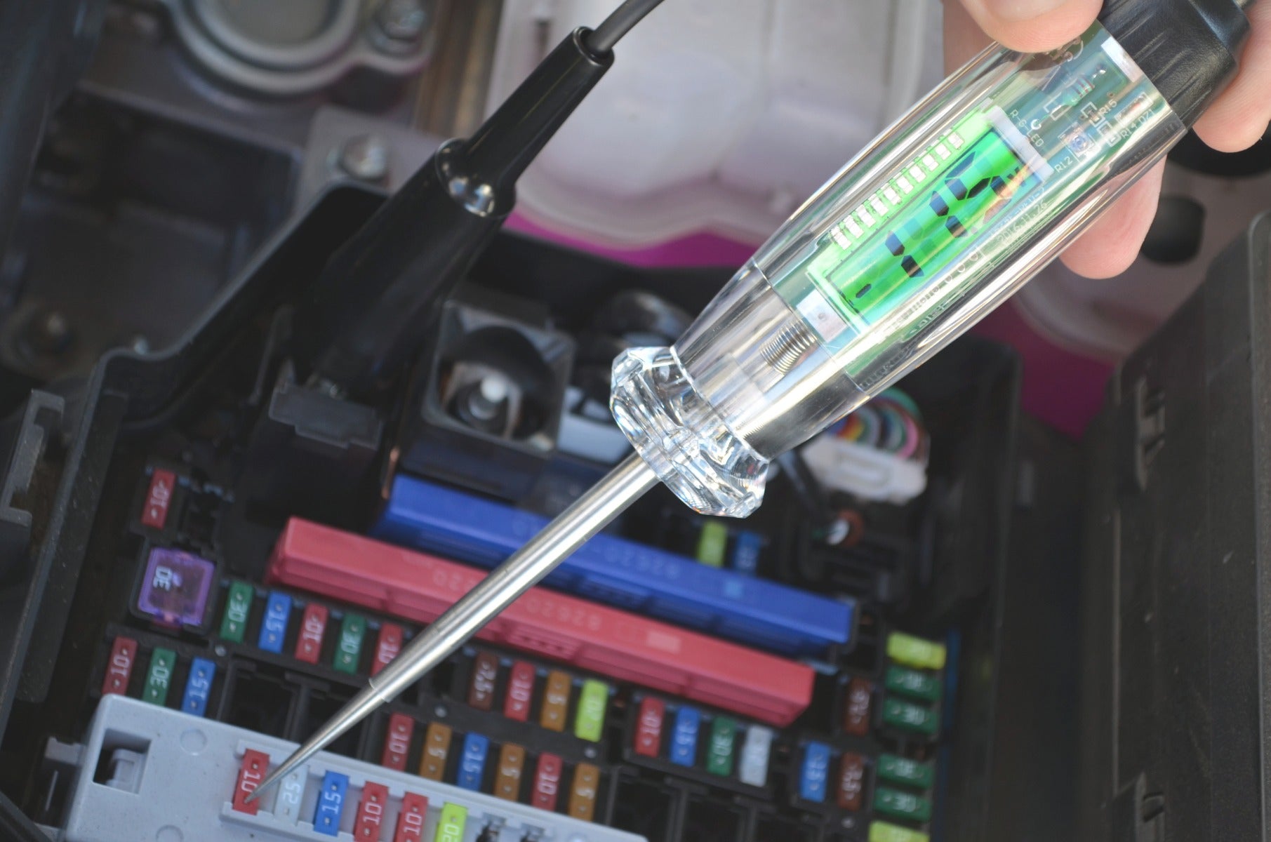 Astro Pneumatic 7767 Digital LCD Circuit Tester in use on automotive fuse box, close-up angle view