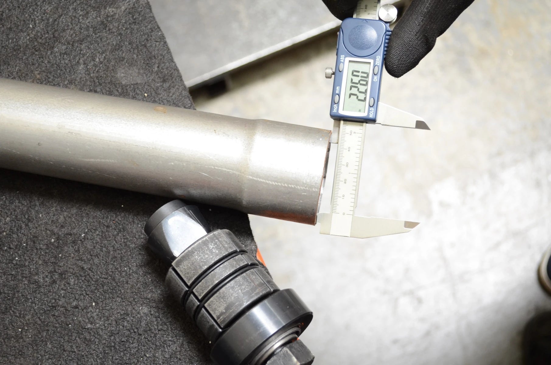 Exhaust pipe stretcher expander tool beside pipe being measured with digital calipers